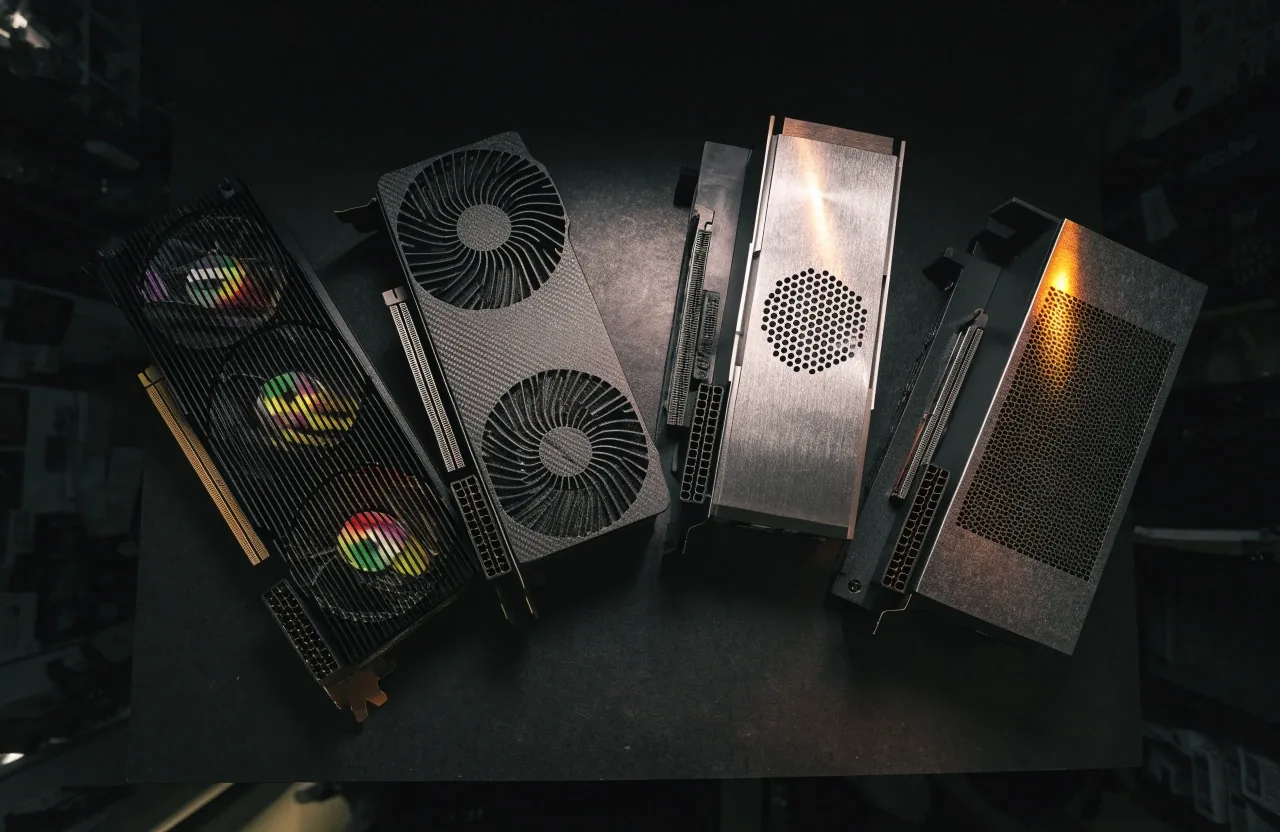 Four midrange graphics cards laid out side by side on a dark workbench under a single warm shop light